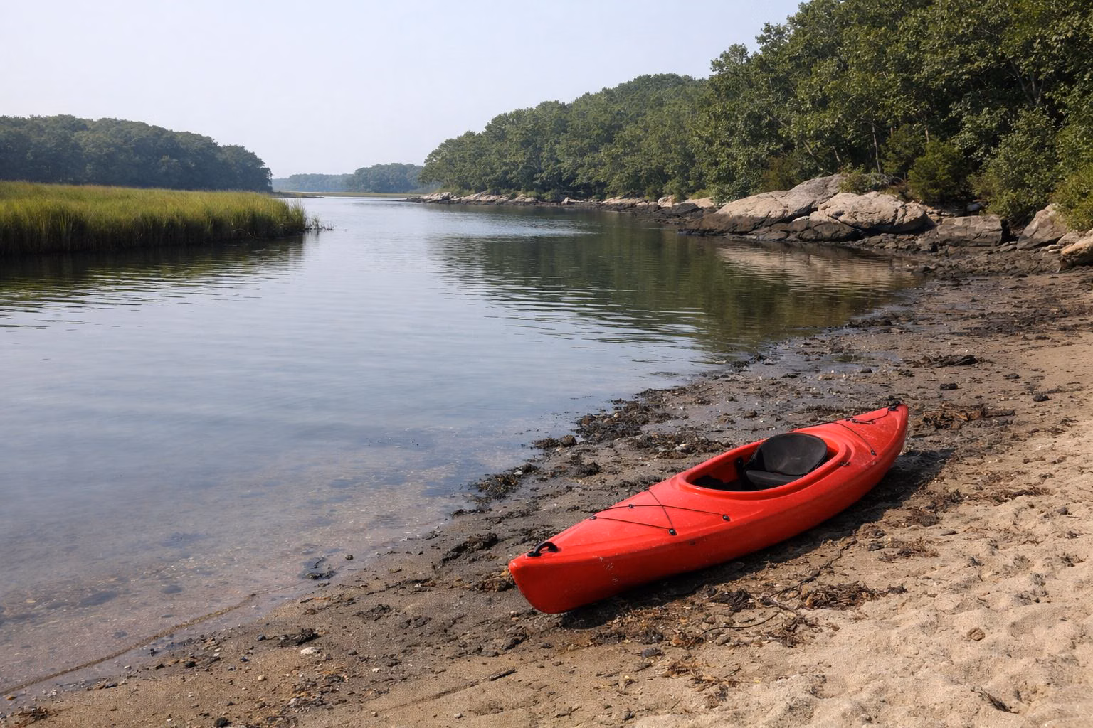 Calm tidal river with marsh banks and a kayak on the shore