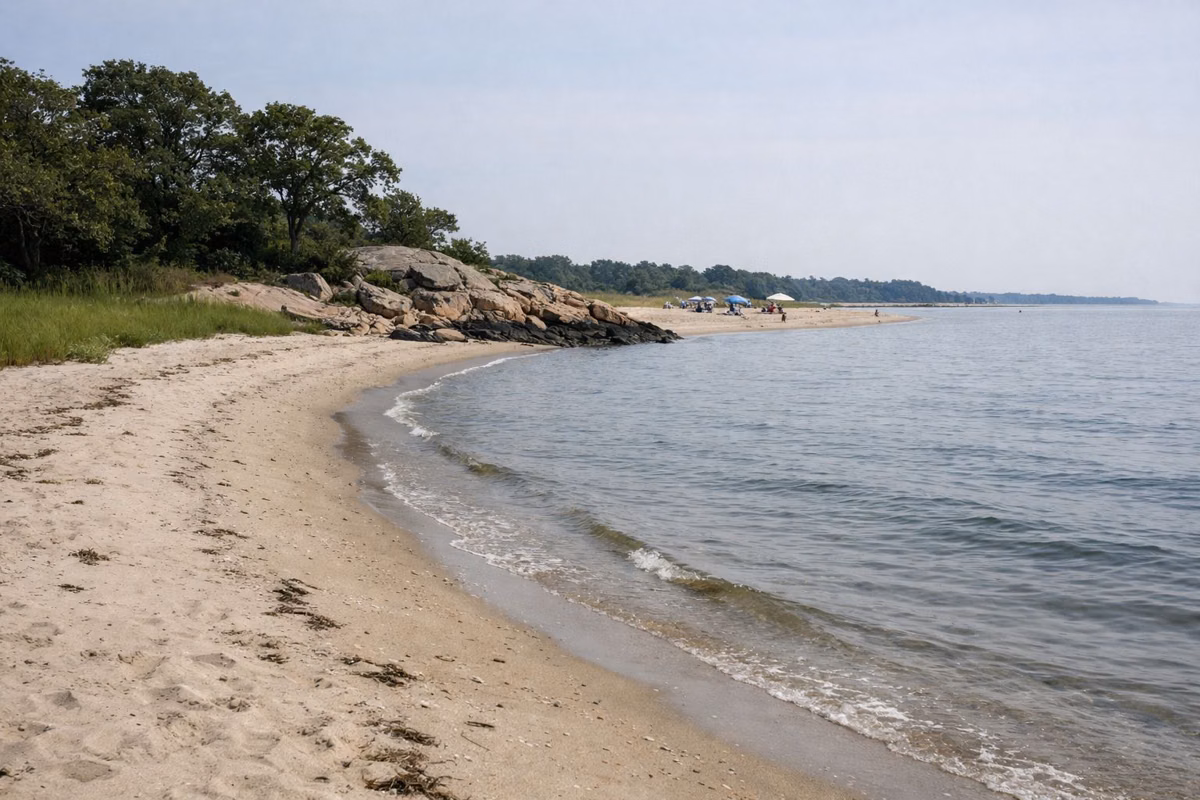 Wide sandy beach curving along a calm Long Island Sound shore in summer