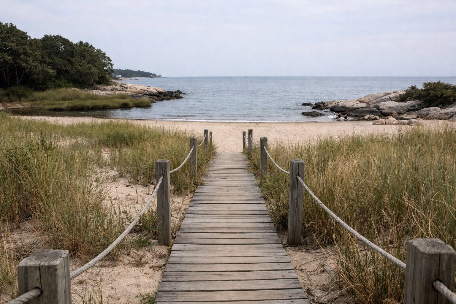 Wooden boardwalk path crossing dune grass toward a beach